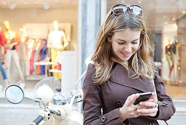 Woman on a scooter checking her phone outside a shop window